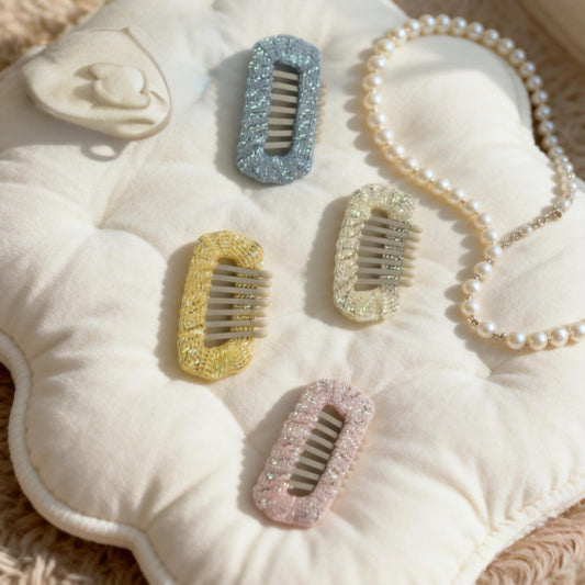 SilkyCo Gold Sequin-Woven Dog Barrettes Party Set. A flat lay of five multi-color (blue, yellow, cream, pink, etc.) barrettes with gold sequin detail and a delicate pearl necklace, arranged on a light quilted mat. Perfect for creating a dazzling party look for your pet.