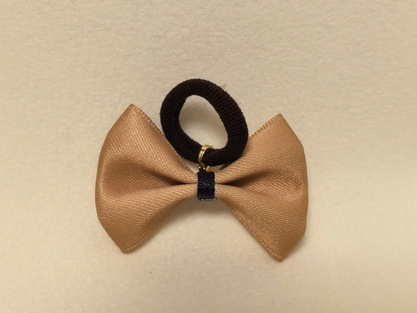 Light tan (beige) pet bow with a black center and attached black hair tie, flat lay presentation. SilkyCo.