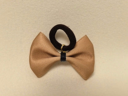 Light tan (beige) pet bow with a black center and attached black hair tie, flat lay presentation. SilkyCo.