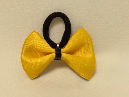 Construction detail of the bright yellow bow, showing the black band and gold connector that holds the elastic hair tie.